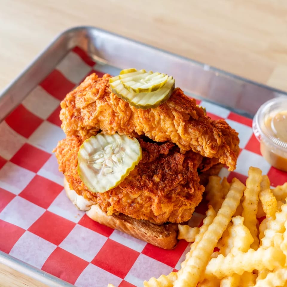 Crispy fried chicken sandwich with pickles, crinkle-cut fries, and dipping sauce on a red checkered tray.