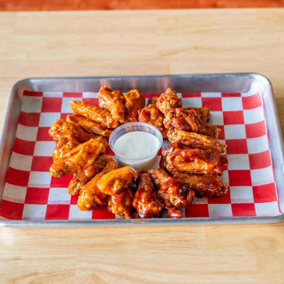 A metal tray of chicken wings in various sauces with a side of ranch dressing.
