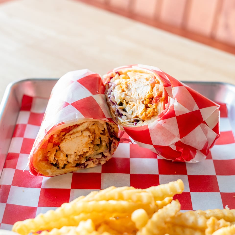 Two chicken wraps in red and white checkered paper, with crinkle-cut fries on a metal tray.
