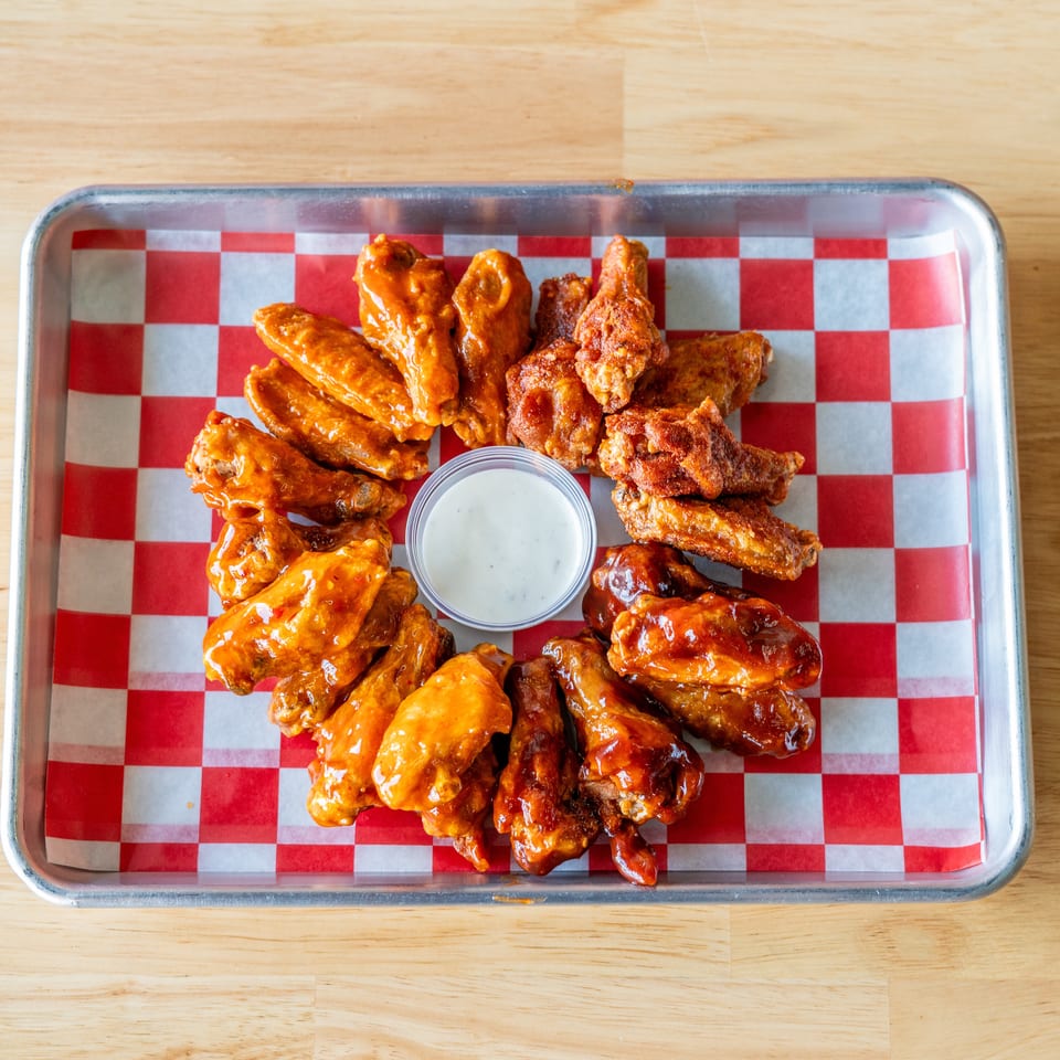 Assortment of chicken wings with various sauces and a side of ranch dressing on a checkered tray.