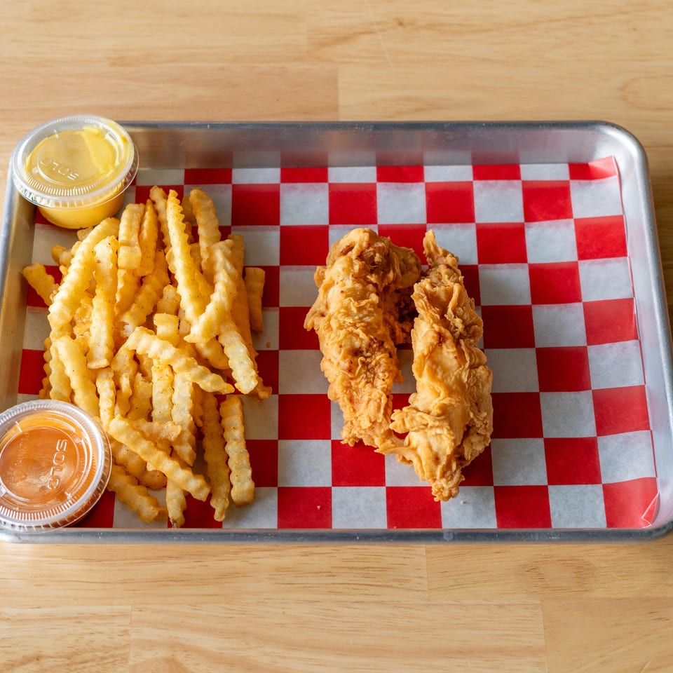 Crispy chicken tenders and crinkle-cut fries with two dipping sauces on a checkered tray.