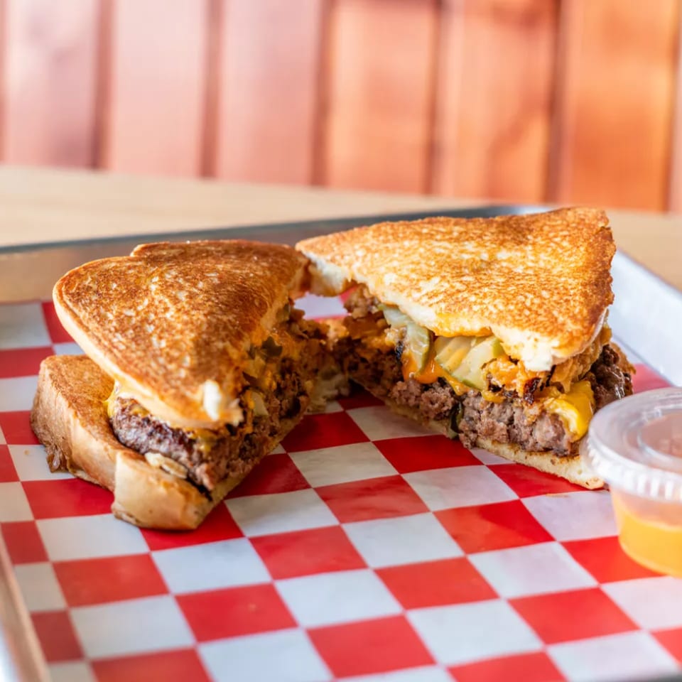 Grilled cheese burger with caramelized onions and cheese on a red and white checkered paper.