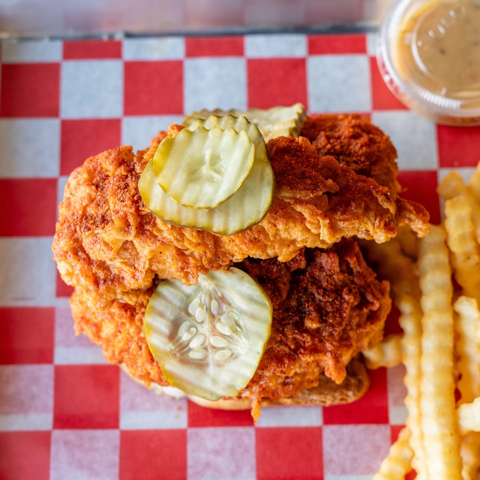 Top-down view of a fried chicken sandwich with pickles, crinkle-cut fries, and dipping sauce.