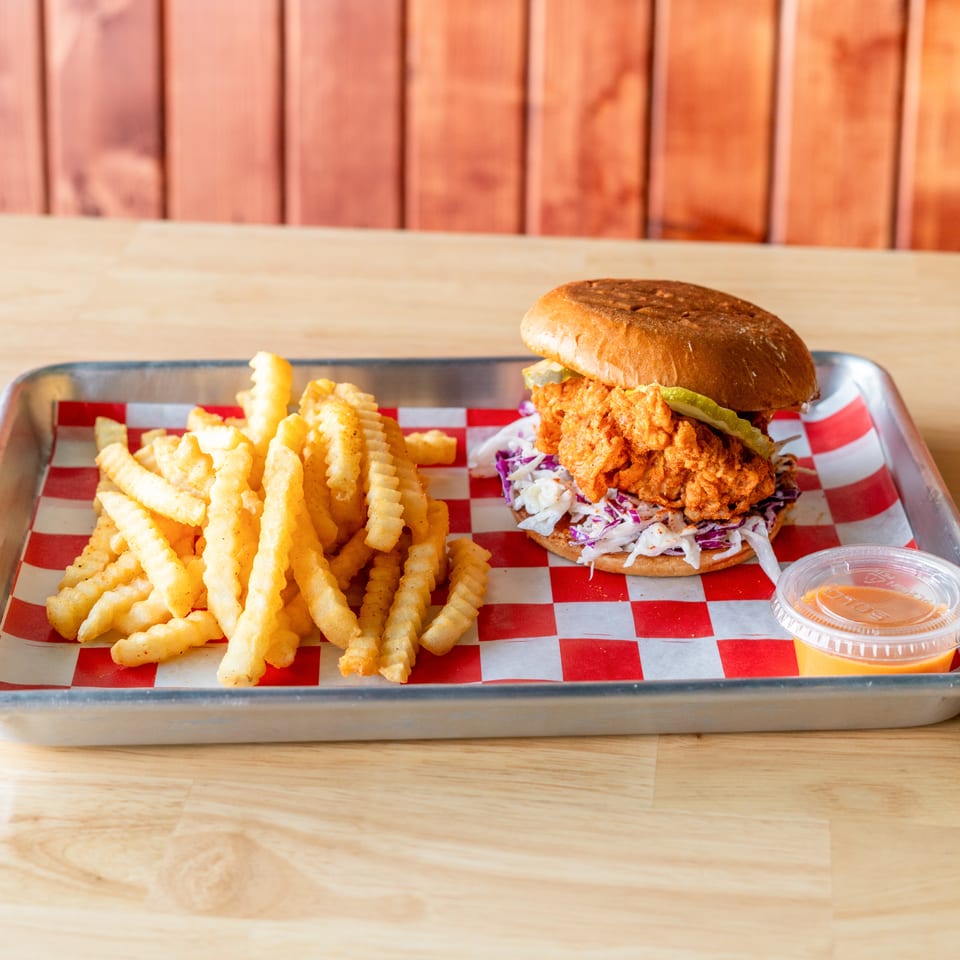Spicy fried chicken sandwich with coleslaw and pickles, served with crinkle-cut fries and sauce.