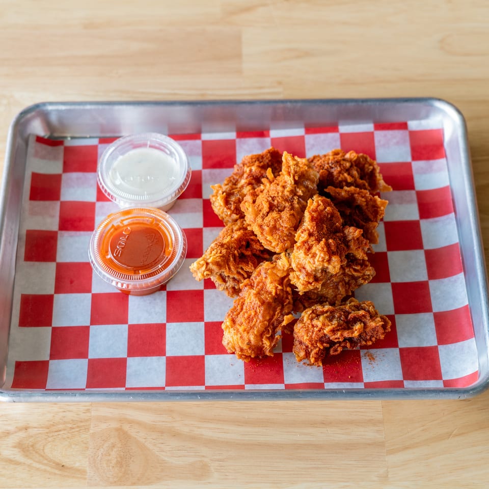 Crispy fried chicken pieces with two dipping sauces on a red and white checkered paper-lined tray.