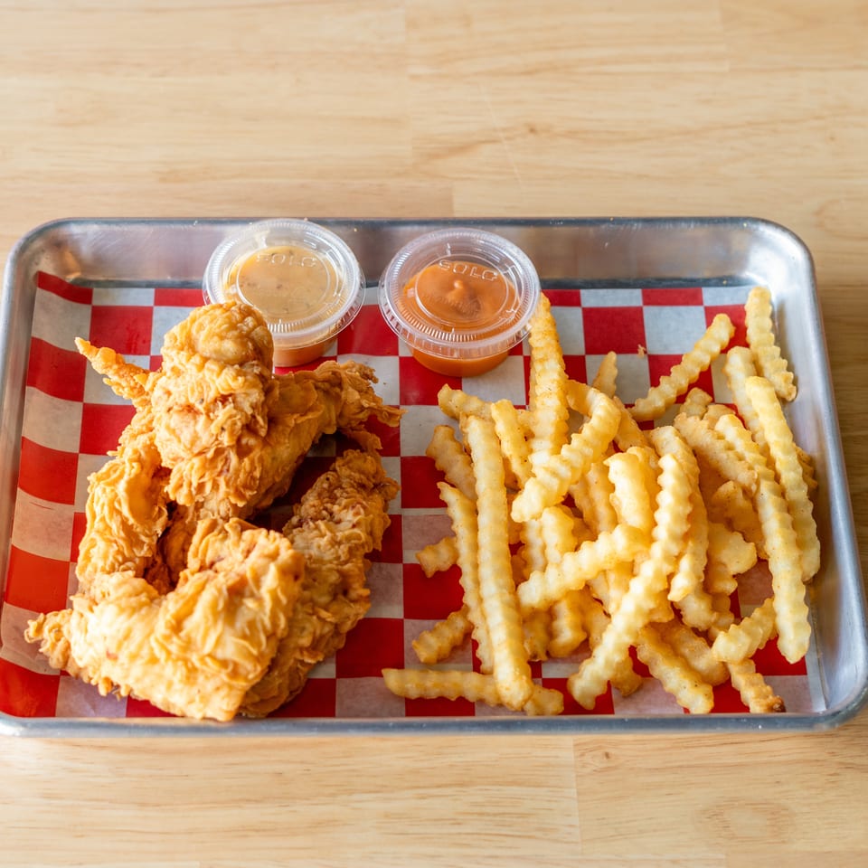 Fried chicken tenders and crinkle-cut fries with two dipping sauces on a metal tray.